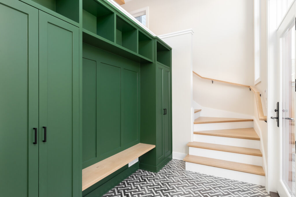 A large foyer with a vibrant green storage unit, white oak bench and stairs, and a black and white pattern tile flooring.